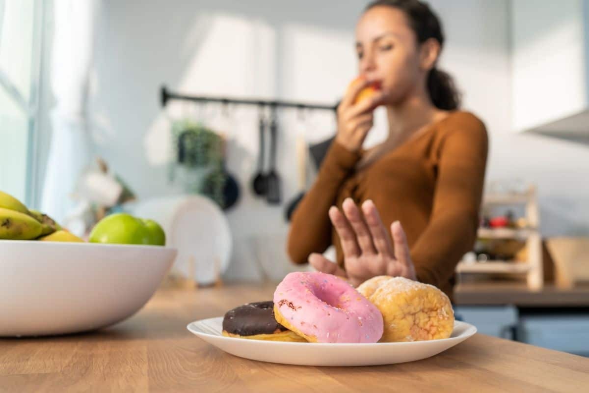 Woman eating a donut while avoiding whitening-sensitive foods after dental treatment.