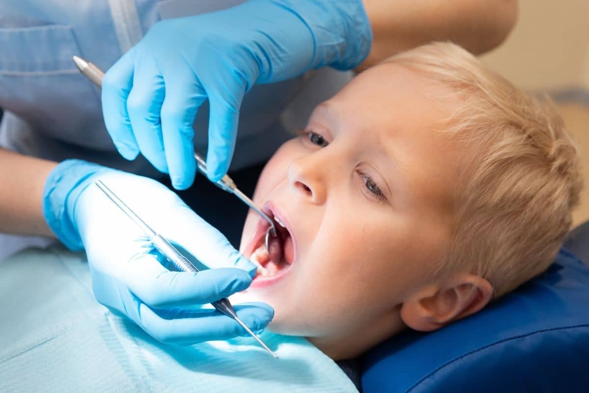 Young child receiving dental examination with dentist using tools to inspect teeth.