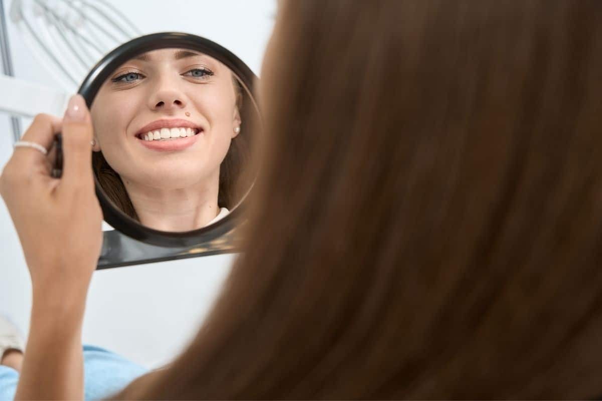 Woman smiling at her reflection in a mirror, displaying her bright teeth and healthy smile.