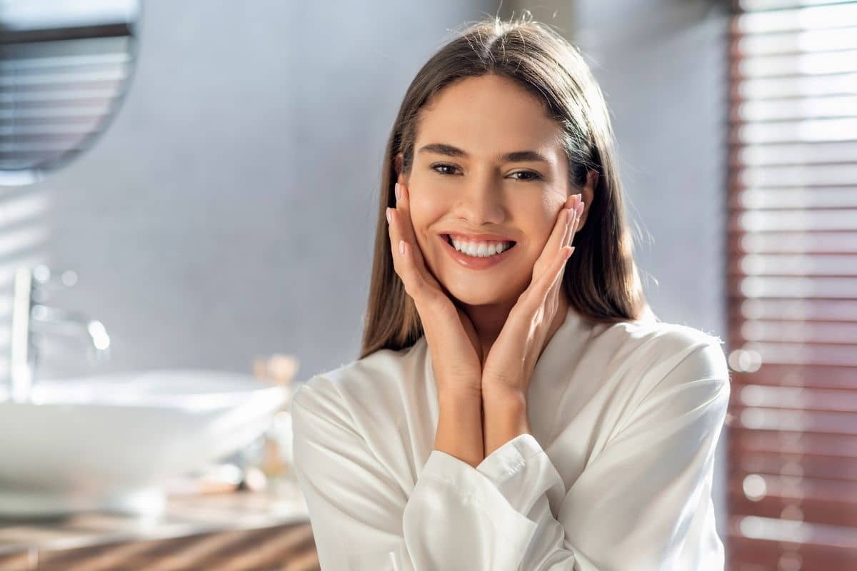 Woman with a bright, healthy smile touching her face in a dental office setting.