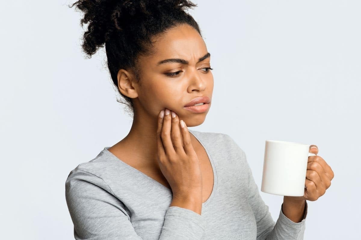 Woman holding mug experiencing jaw pain, illustrating TMJ symptoms requiring dental attention.